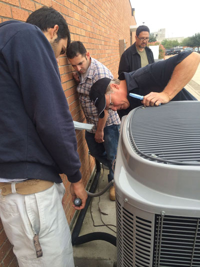 An instructor showing students the back of an outdoor air conditining unit.