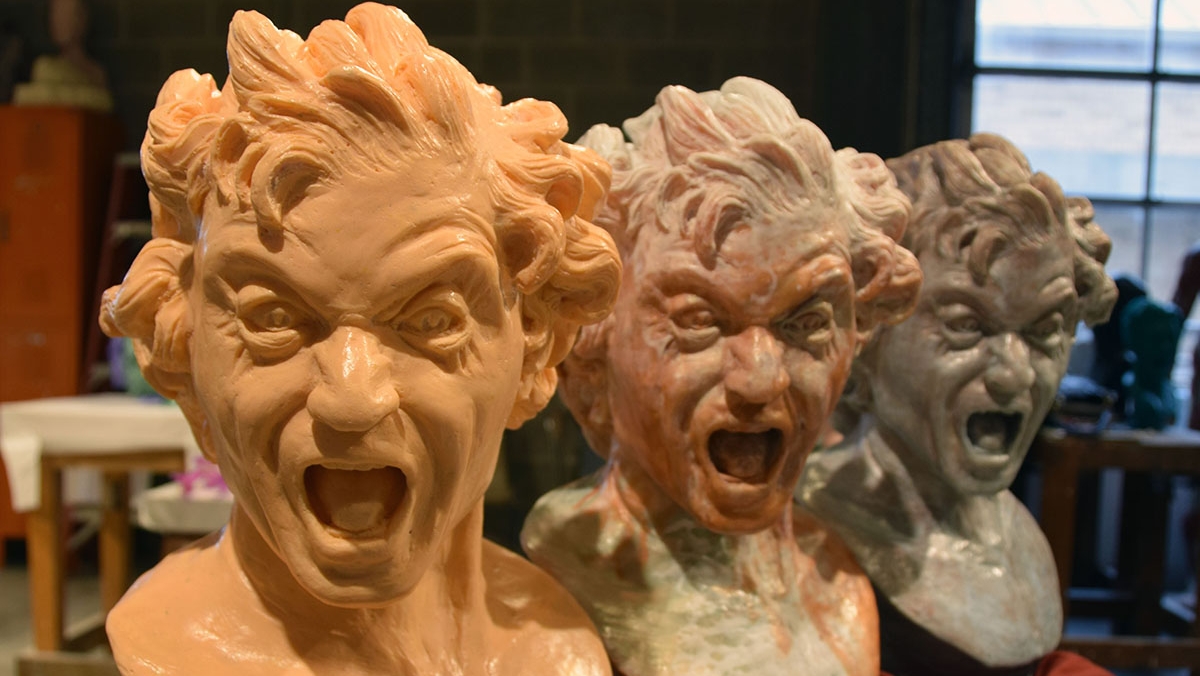 Three sculpted busts of a man yelling are displayed in a row