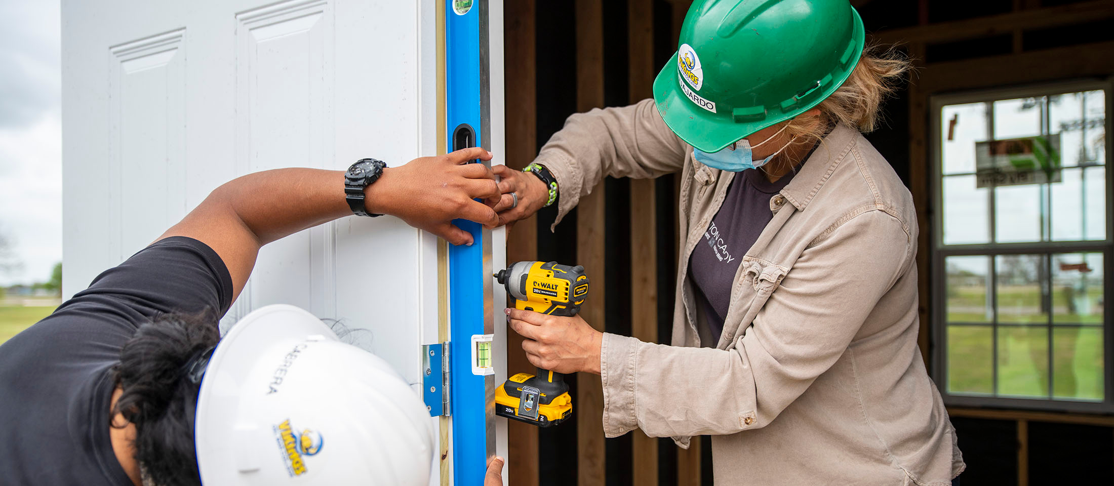 A man and woman wearing hard hats work on a door frame