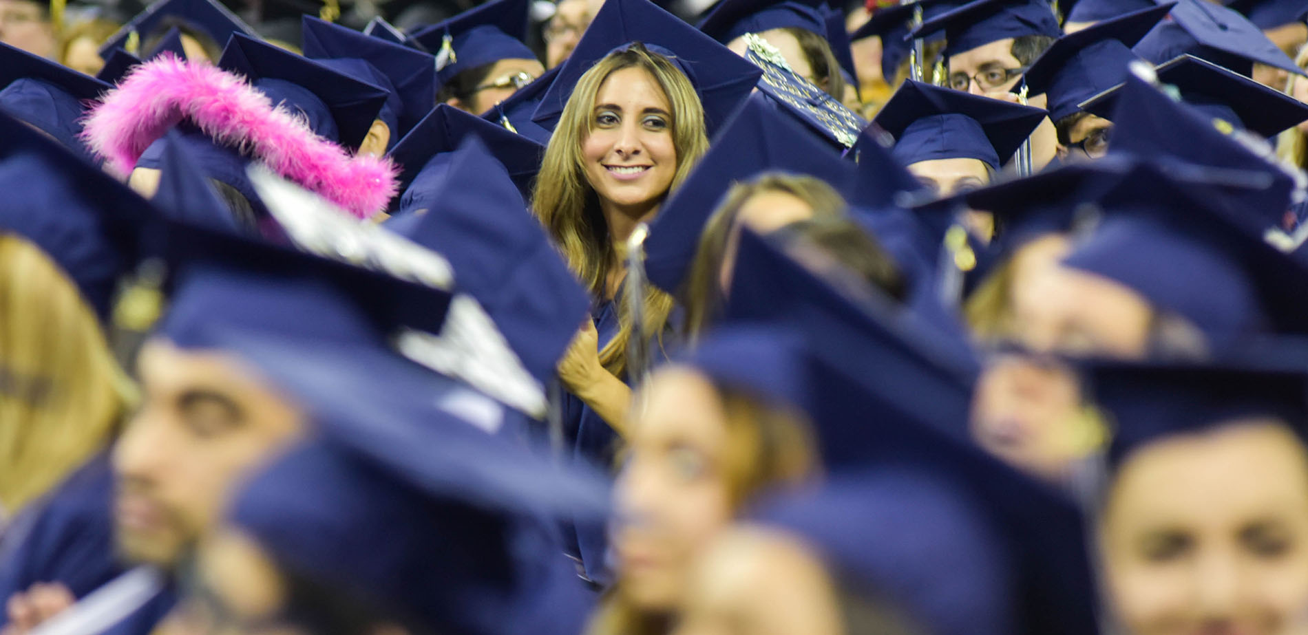 A crowd of college graduates with a female smiling at camera