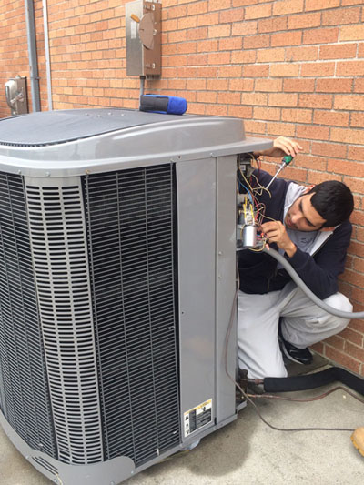 A student working on the wiring on the back of the outdoor air conditioning unit.