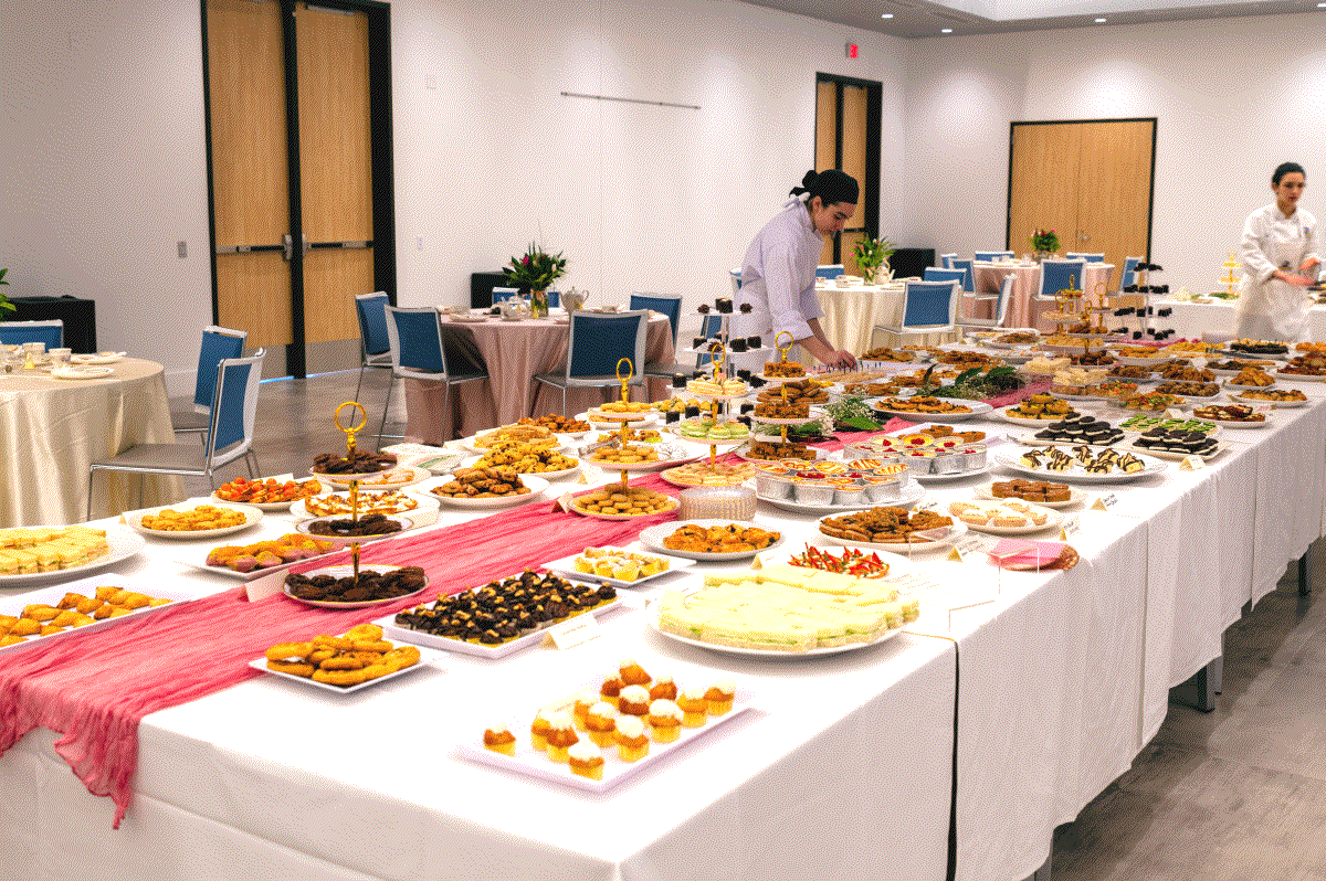 Banquet setup with tables full of diverse pastries and finger foods in a bright room at the annual tea party.
