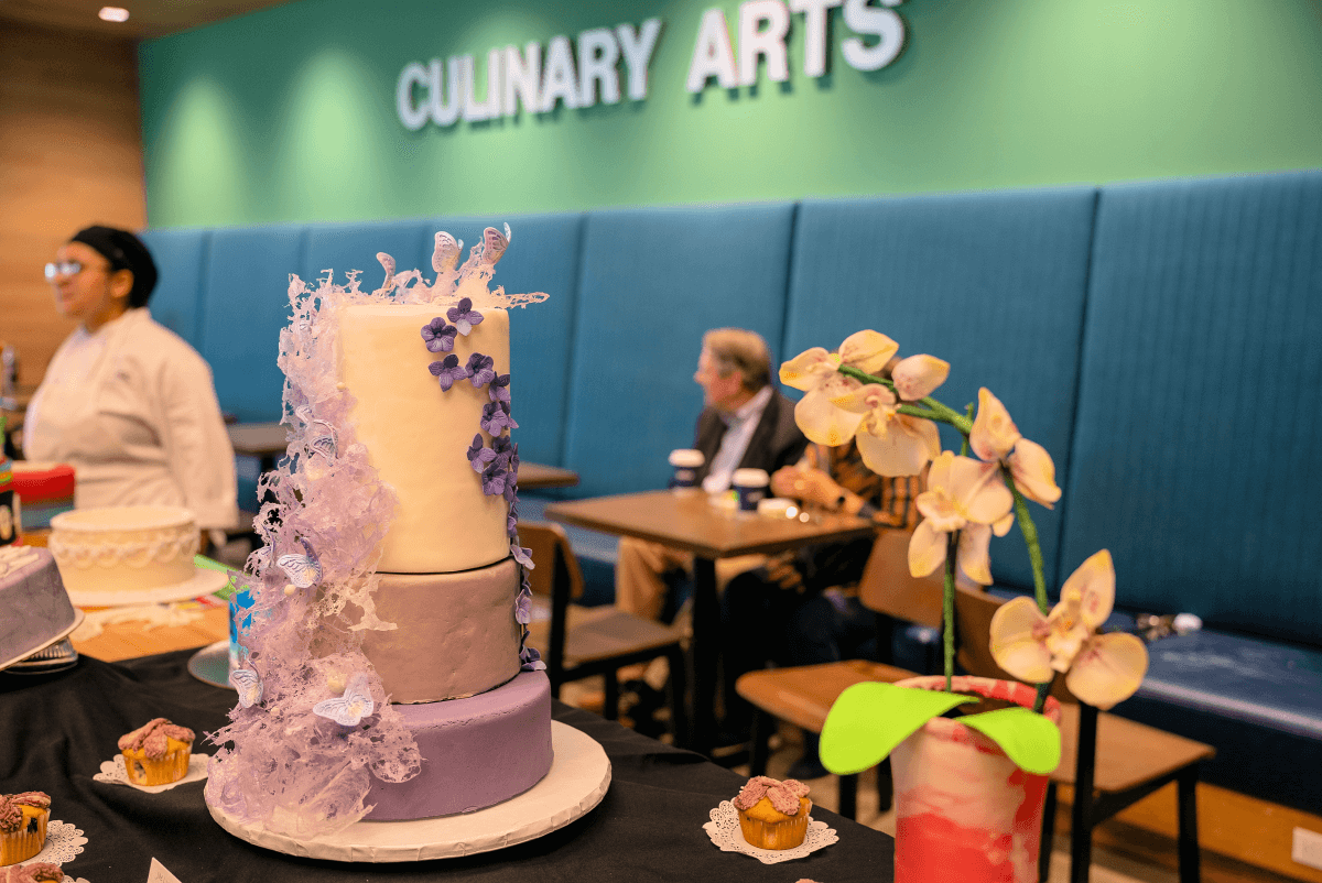 A three-tiered purple cake with floral decorations in the culinary arts building.