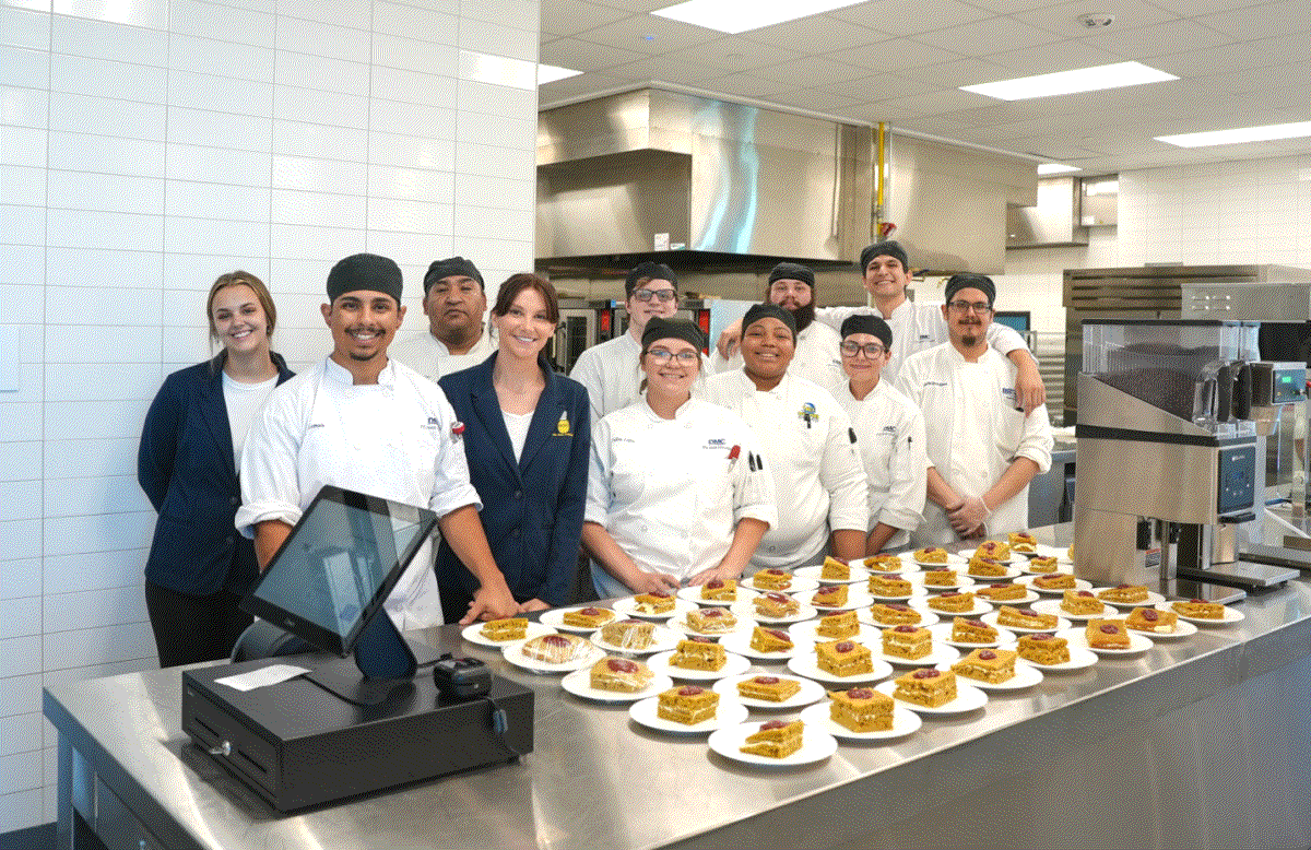 Group of student chefs in a kitchen classroom with plated dishes.