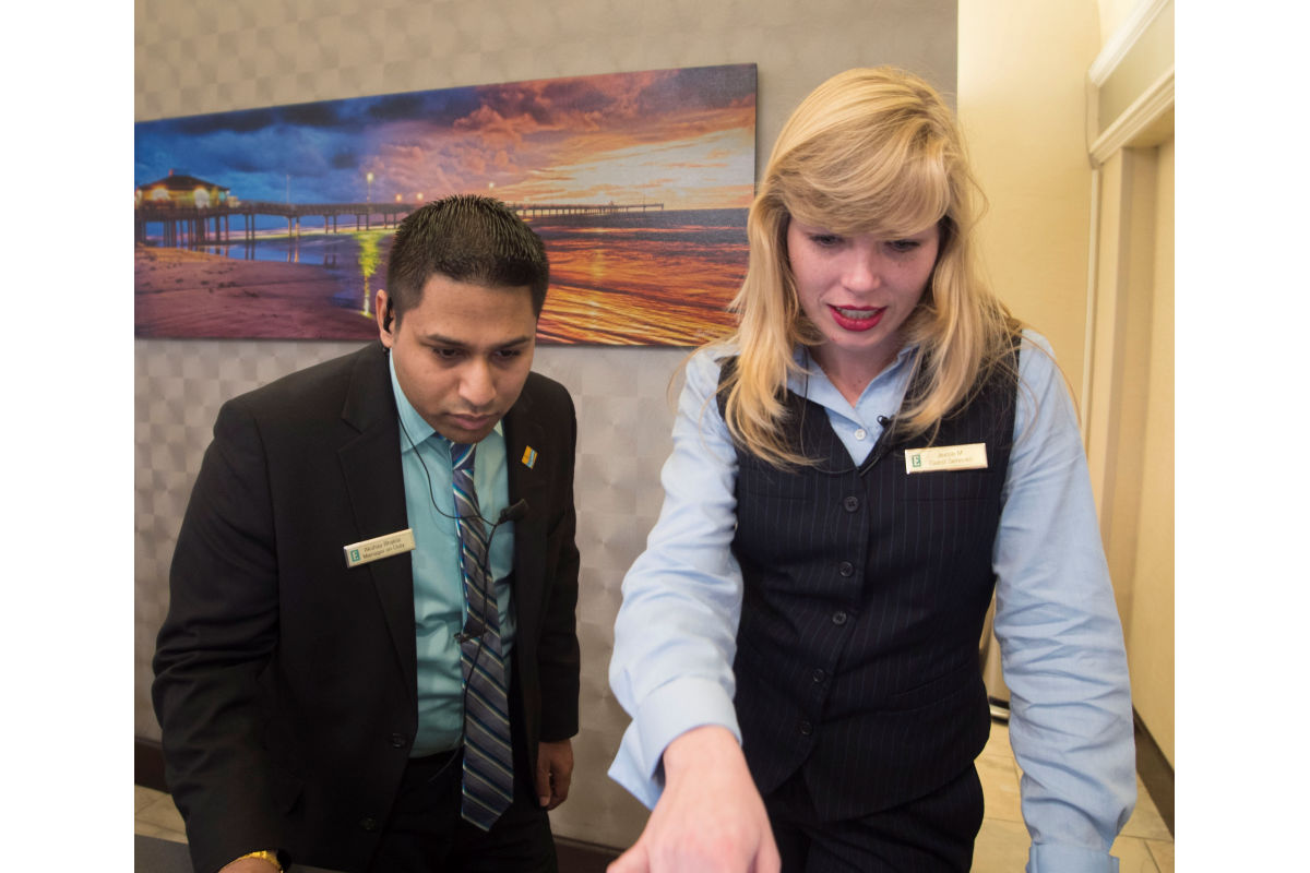 Male hospitality student works with hotel employee at front desk