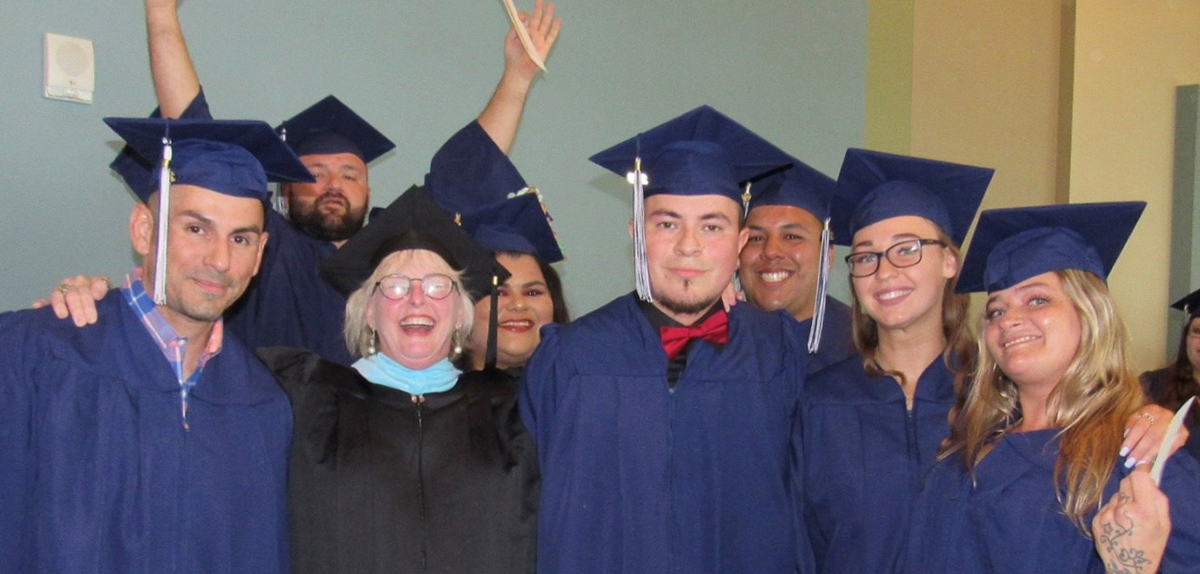 A group of May 2019 graduates smile for the camera in their caps and gowns.