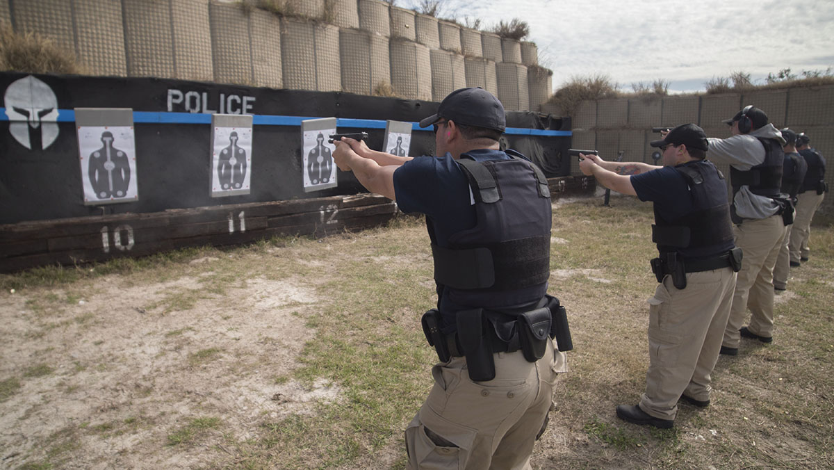 Trainees in protective gear shoot at targets