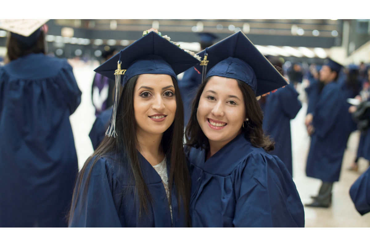 Students Sarai Morua and Sabrina Coleman smile and pose together in their graduation caps and gowns