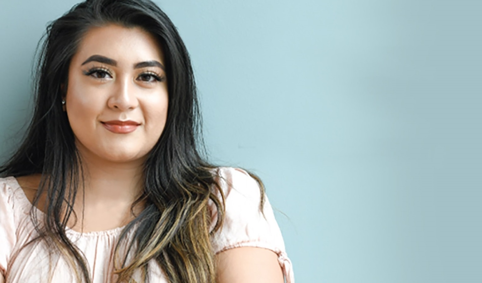 Young woman smiling against a teal background.