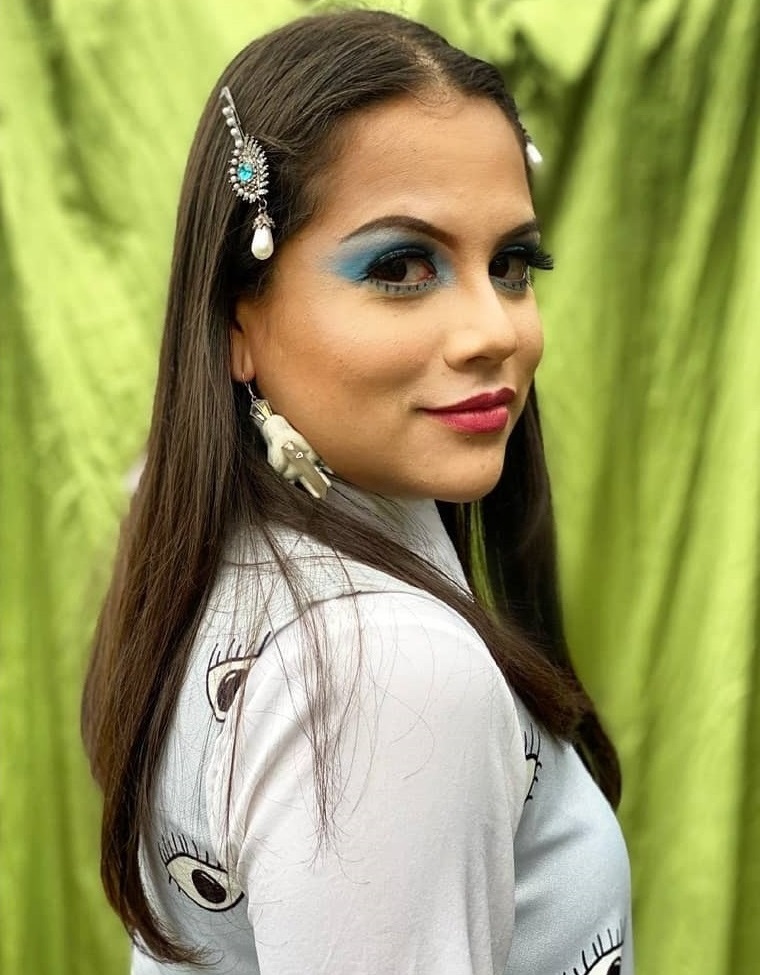Mayra Zamora in colorful makeup, smiling over her shoulder.