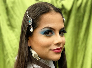 Mayra Zamora in colorful makeup, smiling over her shoulder.