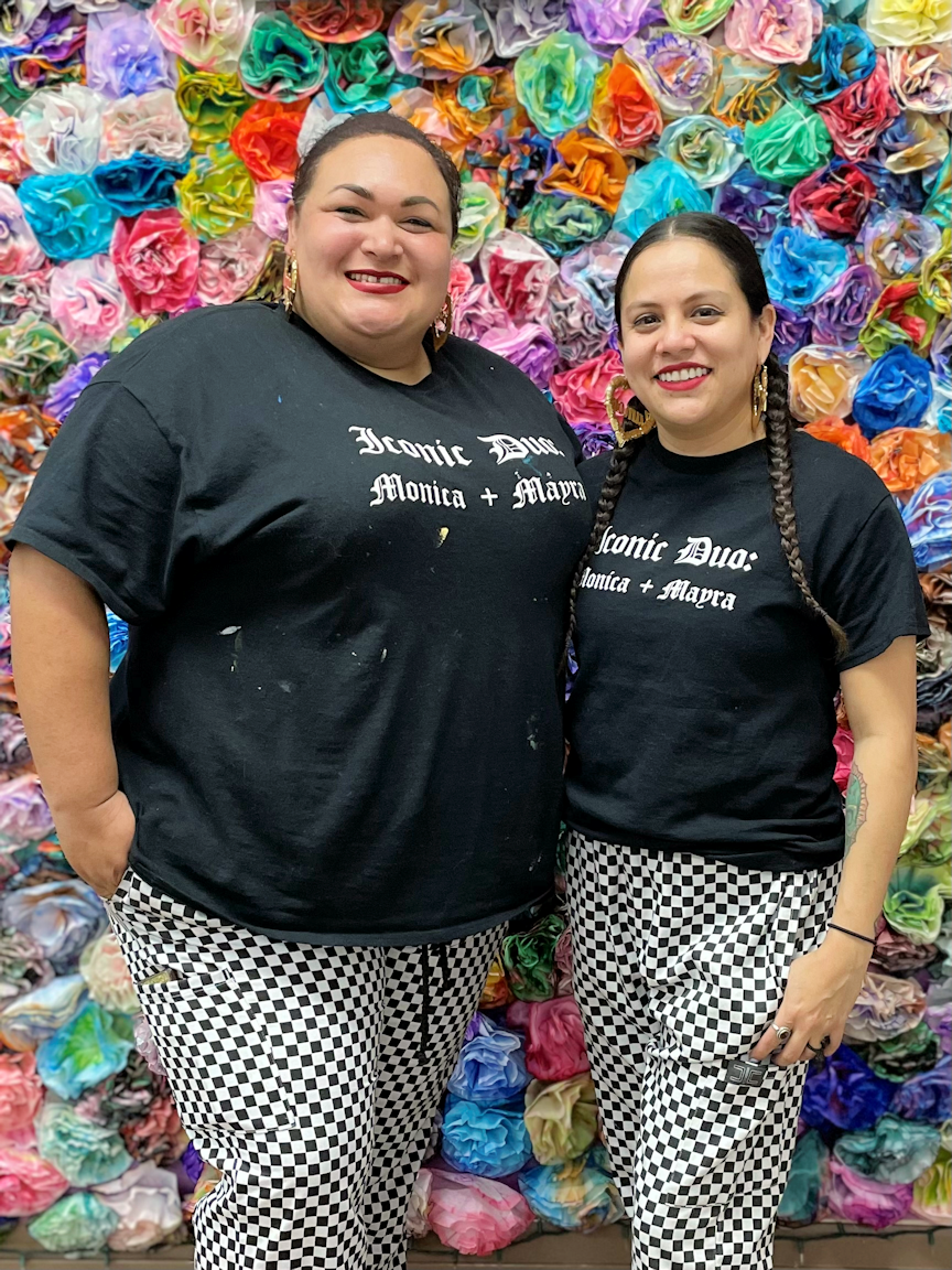 Monica and Mayra in front of a flower wall