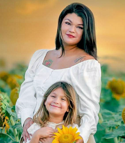 Aundrea Salinas Brasier and her daughter Audrey against a sunset backdrop in a field of sunflowers.