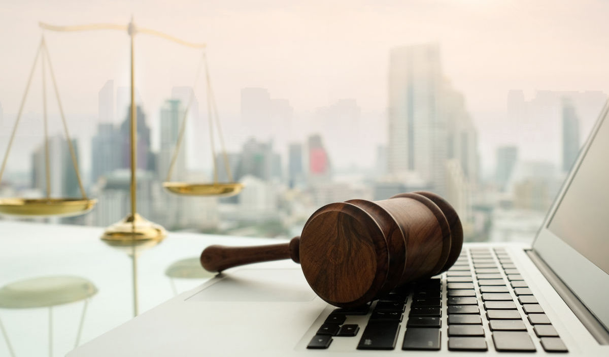 Photo of a gavel, laptop computer, and scales of justice on a desk overlooking a cityscape