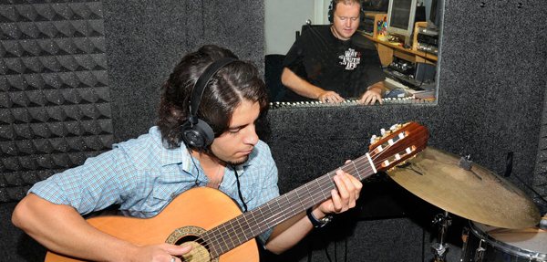 A sound recorder is playing his guitar inside a recording studio.