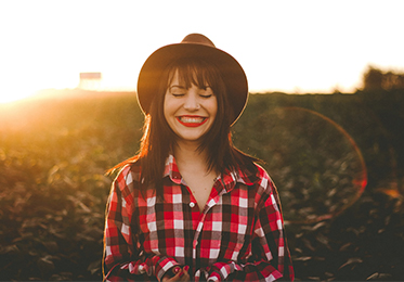 Smiling female student with eyes closed and hat on in a field