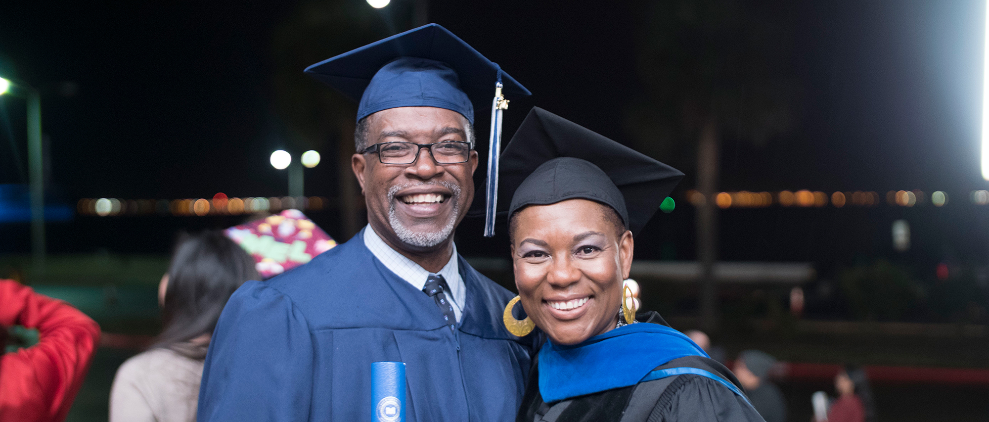 A man and woman smile and pose in their graduation caps and gowns