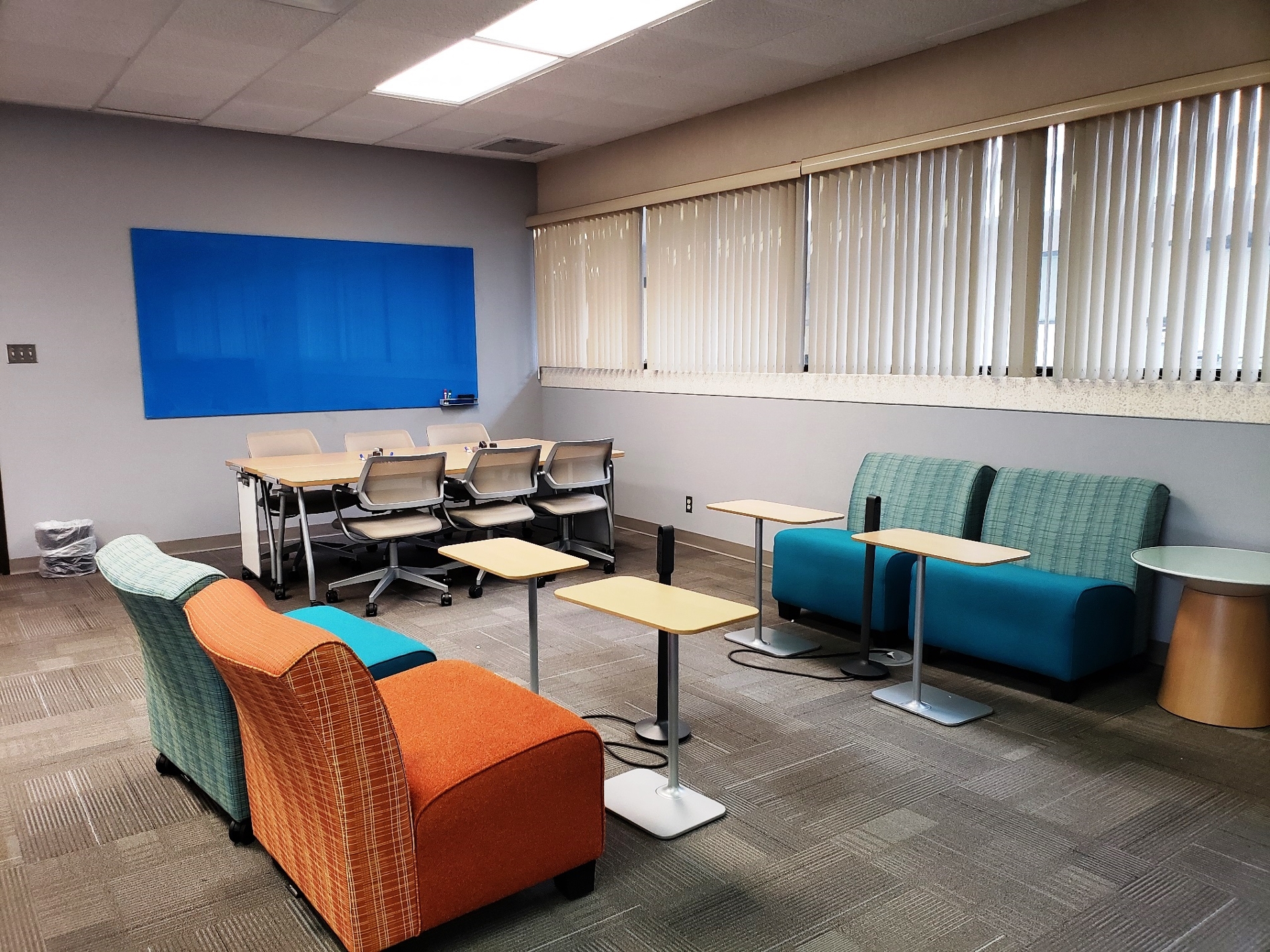 Corner of main Collaboratory room with various sized tables/chairs and a dry erase board.