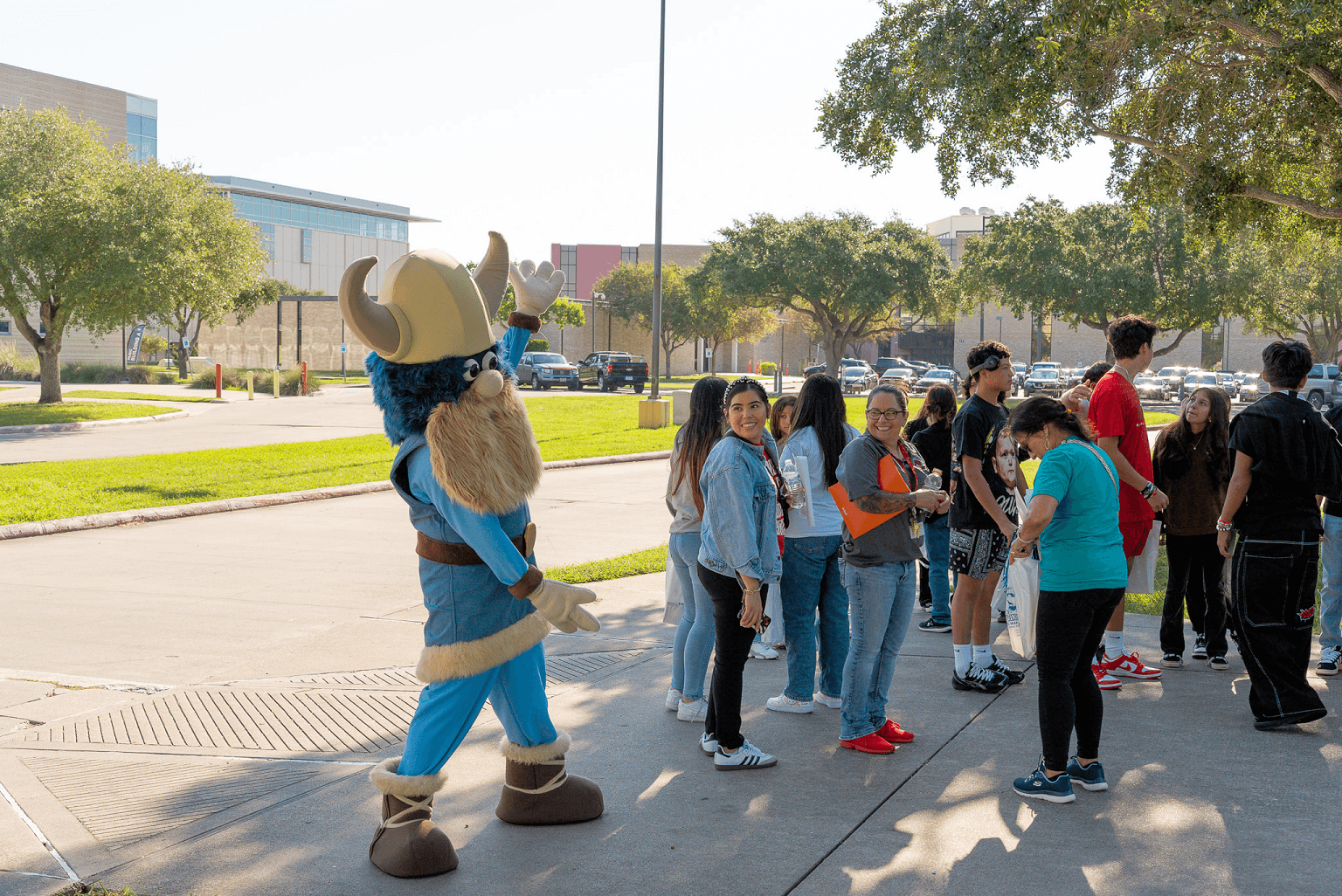 Valdar the Viking campus mascot approaches a group of people gathered on a sunny sidewalk.