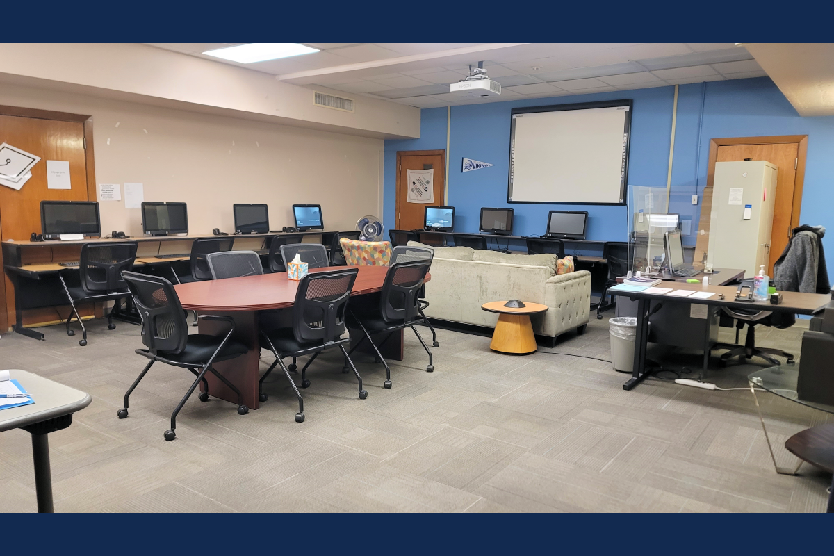 Heritage Campus Veterans' lounge with desks, chairs, computers, a sofa, and a projector screen.
