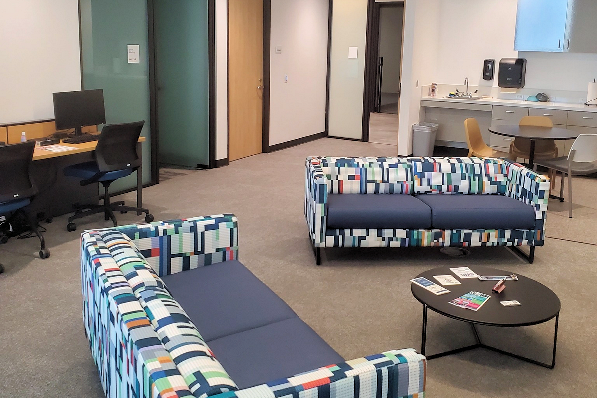 Oso Creek Campus Veterans' lounge area with patterned sofas, a coffee table, and a desk with computer monitors.