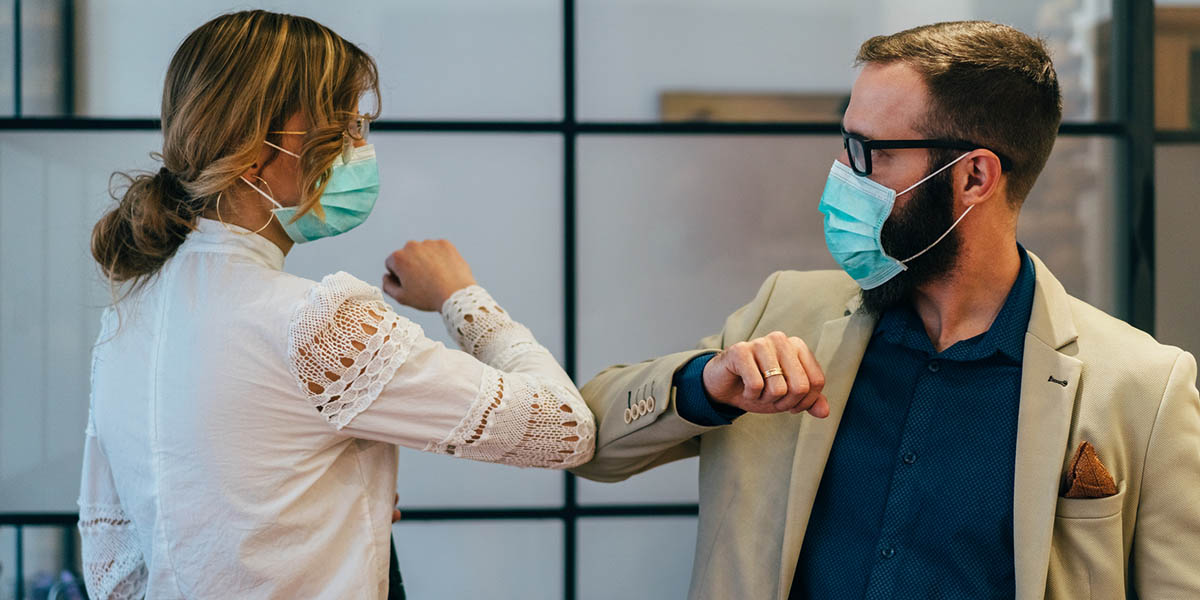 Man and woman wearing face masks and exchanging an elbow bump