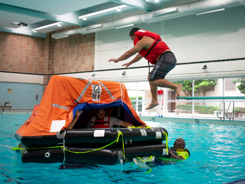 man jumping into rescue raft for maritime safety pool training